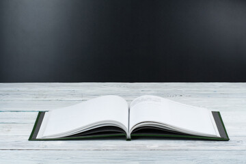 Open book on wooden deck table and black board background. Back to School. Education concept with copy space for your ad text.