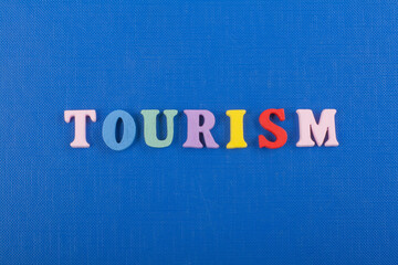 TOURISM word on blue background composed from colorful abc alphabet block wooden letters, copy...
