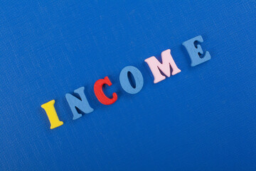 INCOME word on blue background composed from colorful abc alphabet block wooden letters, copy space...
