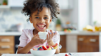black child having breakfast eating yogurt with fresh fruit, sitting at the kitchen table. Healthy...