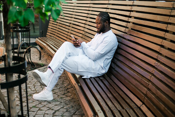 African American hipster guy in cultural and ethnic clothing dashiki chatting on smartphone...