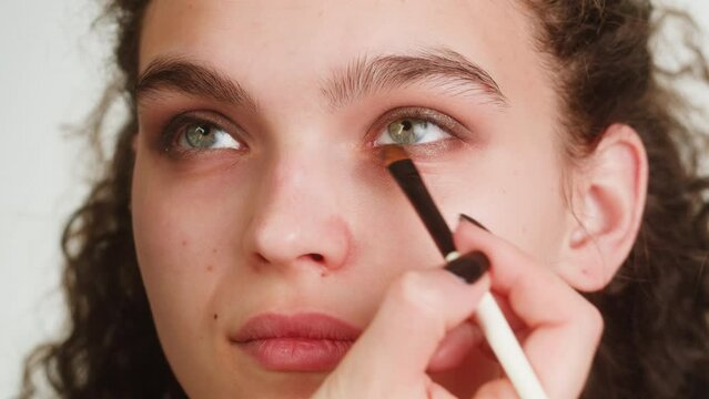 Eye shadow makeup to the upper eyelid, close-up. Makeup artist applies a bright eye shadow with a make-up brush.Tutorial master class of professional makeup, smoky eyes 