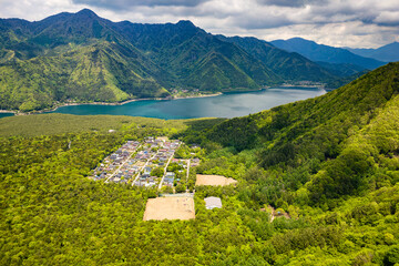 Small village surrounded by lush forest and rugged mountains next to a lake (Saiko, Japan)