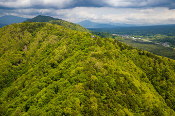 Aerial view of a mountain ridge covered in lush green forest next to a lake (Lake Saiko)