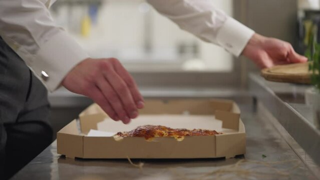 Nearby a guy waiter in a long white shirt puts the finished cheese cake in a square cardboard box and ties it with string to send to the client