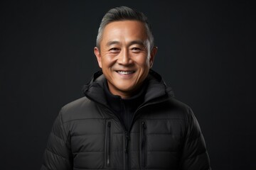Obraz premium Portrait of a smiling asian man in his 50s donning a durable down jacket isolated on modern minimalist interior