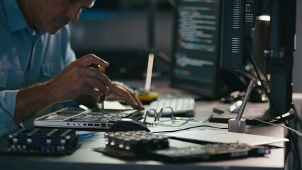 Close up of male electronics engineer using screwdriver to take laptop to pieces for repair with low key lighting - shot in slow motion