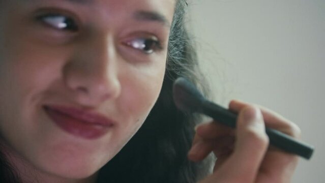 Girl applying blusher to her face with a makeup brush