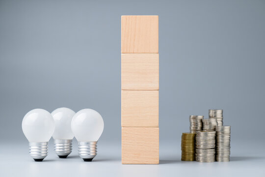 Light bulbs and heap of coins, with stack of wood cubes as the wall between it, the money that is on the other side of the crative idea, making money concept