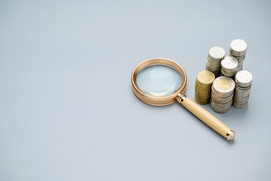Magnifying glass and heap of coins on gray background, take a close look at money concept, reward or benefits, revenue, and income, financial status, search a finance resource