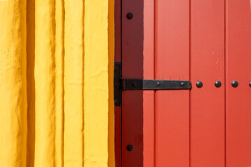 Detail of a traditional red wooden door with black metal hinge on a yellow wall