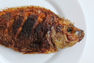 Fried gourami fish on a white plate, isolated on white background, flat lay or top view
