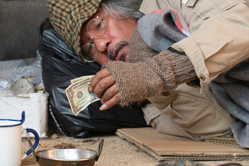 A homeless man clutches a one dollar bill in his hands