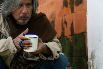A beggar holds a cup in his hands and gazes at the camera with a serious expression.