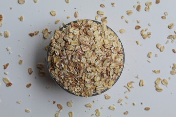 Rolled oats in transparent glass bowl, isolated on white background, flat lay or top view