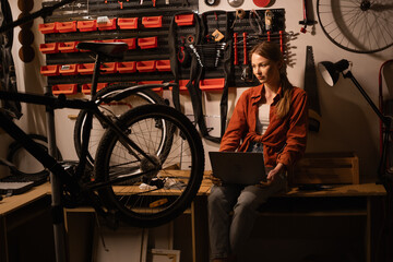 Female mechanic in her Workshop or garage looking at laptop. Bike shop owner with laptop.