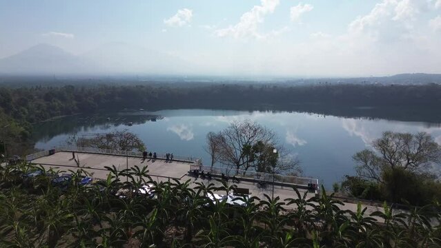 Concrete viewing deck in a rural area that runs alongside a serene lake, which is surrounded by dense forests of Lake Tikub, Tiaong, Quezon, Philippines. Drone aerial shot