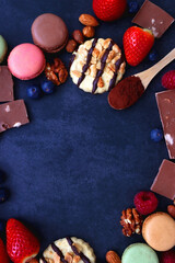 Macarons, chocolate, cookies, berries and various nuts on dark blue background. Top view.