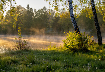 Fog illuminated by rays of rising sun over ponds