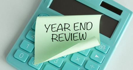 Selective focus of calculator, pen and a stack of memo notes written with Year End Review on a...