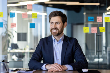 A professional man in a blue suit and white shirt, smiling confidently in a bright, contemporary...