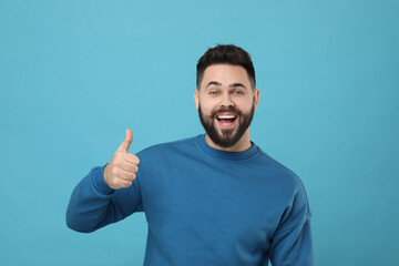 Happy young man with mustache showing thumb up on light blue background