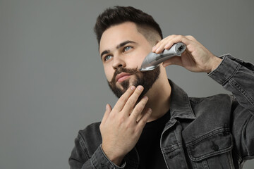 Handsome young man trimming beard on grey background. Space for text