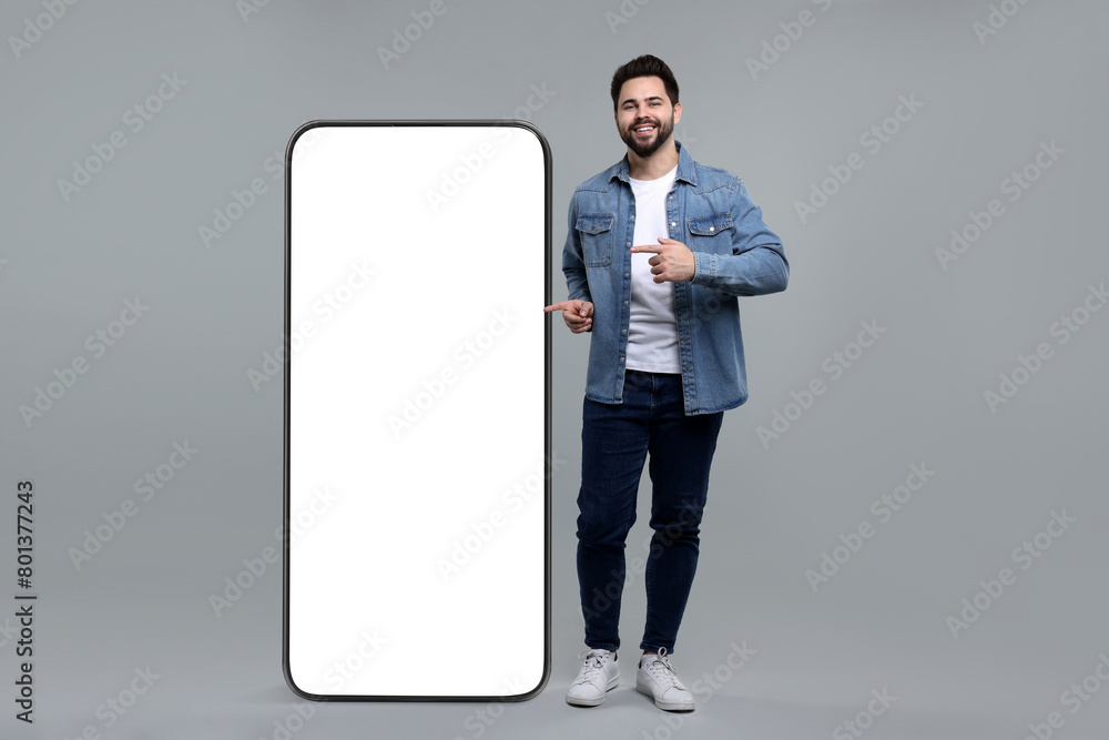 Aufkleber man pointing at huge mobile phone with empty screen on grey background. mockup for design