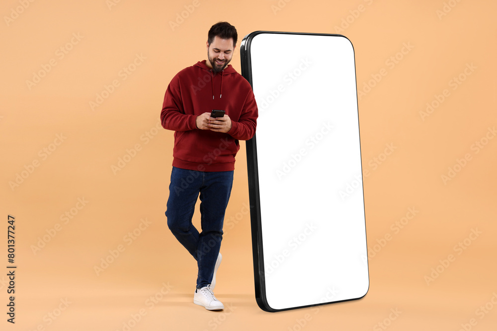 Aufkleber man with mobile phone standing near huge device with empty screen on dark beige background. mockup f
