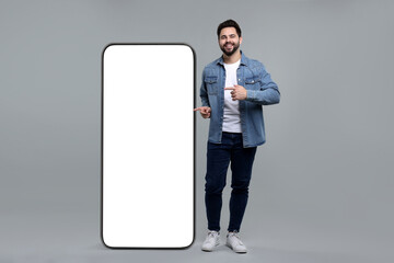 Man pointing at huge mobile phone with empty screen on grey background. Mockup for design
