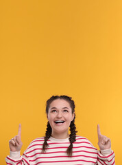 Smiling woman with braces pointing at something on orange background. Space for text