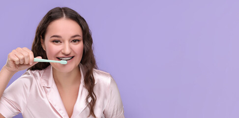 Woman with braces cleaning teeth on violet background. Banner design with space for text