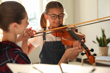 Young woman teaching little girl to play violin indoors