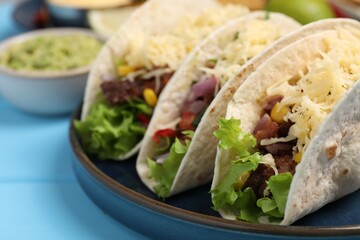 Delicious tacos with meat and vegetables on light blue table, closeup