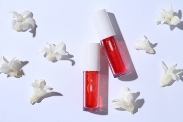 Bright lip glosses and flowers on white background, flat lay