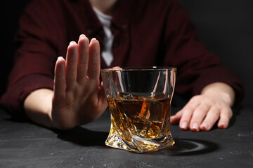 Alcohol addiction. Woman refusing glass of whiskey at dark textured table, closeup