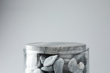 Presentation for product. Glass container with stones on light grey background. Space for text
