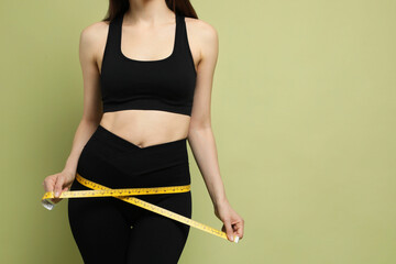 Woman with measuring tape showing her slim body on green background, closeup. Space for text