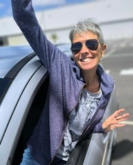 Photographic portrait of a young adult woman, with short hair and sunglasses, leaning out of the...