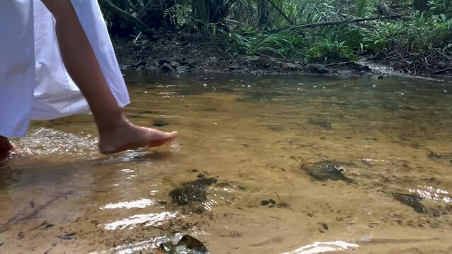 close-up of woman in white dress walking by the river. Feet in the water for spiritual healing