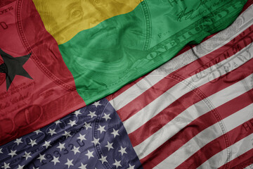 waving colorful flag of united states of america and national flag of guinea bissau on the dollar...