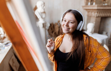 Girl artist paints a picture in a beautiful studio. Female with headphones listening to music.