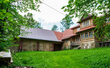 Fototapeta na wymiar In the small village of Poronin in Poland lies this old farm house. The main wooden building is beautiful and surrounded by green grass and trees.
