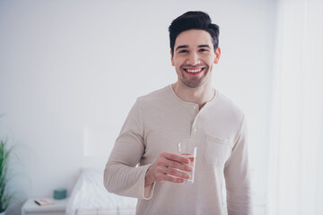 Photo of cheerful nice man drinking water early morning in cosy flat white day light room interior...