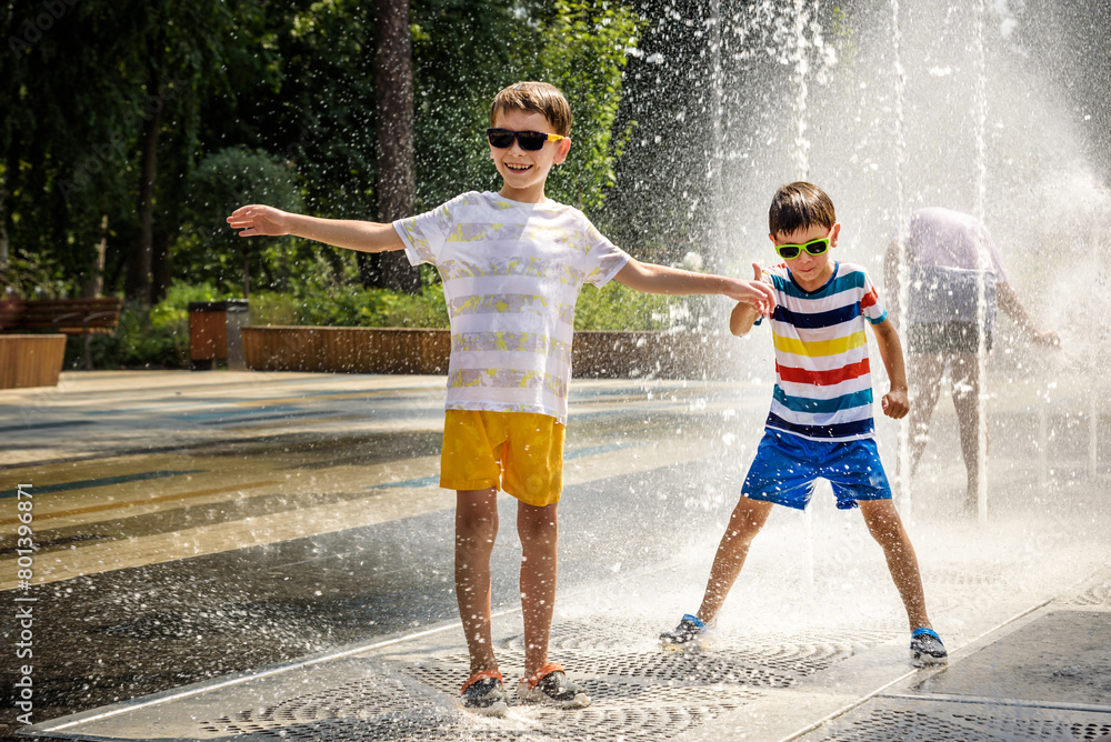 Poster Boy having fun in water fountains. Child playing with a city fountain on hot summer day. Happy kids having fun in fountain. Summer weather. Active leisure, lifestyle and vacation