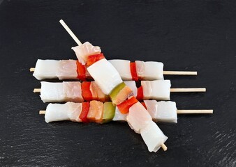 Raw fish skewers with peppers on black slate cutting board.
