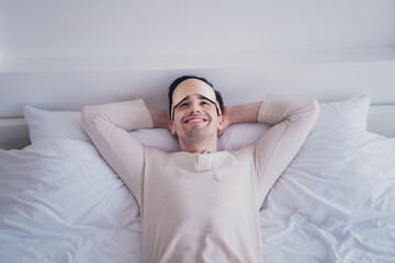 Photo of dreamy happy cheerful man enjoying lying in soft bed white room interior inside