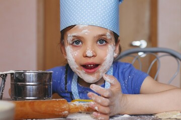 5 year old funny girl in casual and dressed as chef in home kitchen laughs and showing her face...