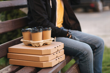  Delivery boy sit on bench and wait for customer. Delivery service. Pizza and coffee