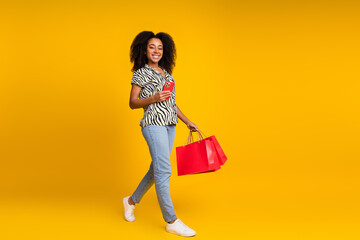 Photo of young woman addicted shopaholic curly hair in zebra print shirt and jeans using phone order clothes isolated on yellow color background